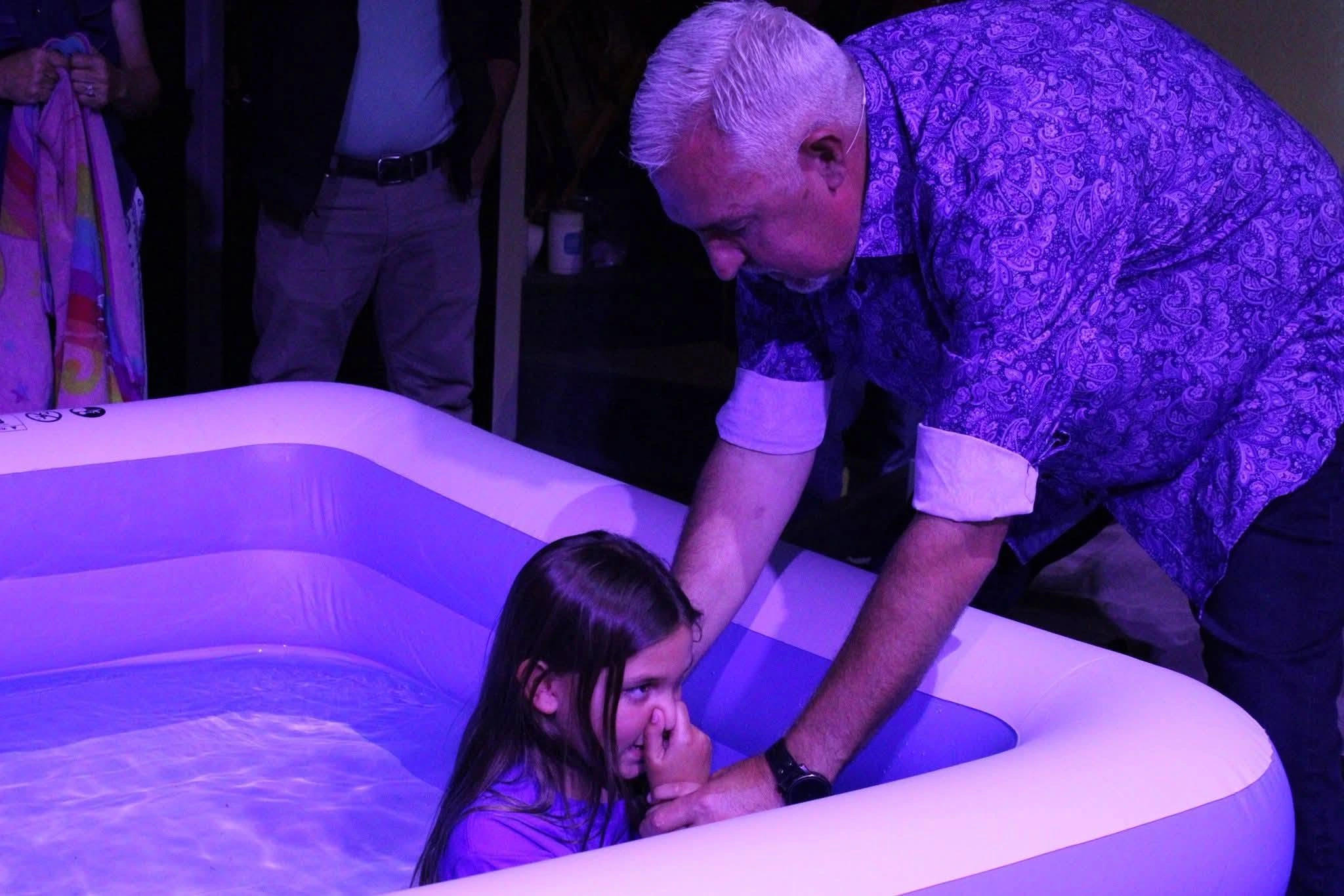 A baptism at The Refuge beneath violet sanctuary light.