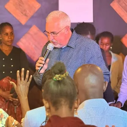 Pastor Larry Goodwin speaking and praying among friends during a mission gathering.