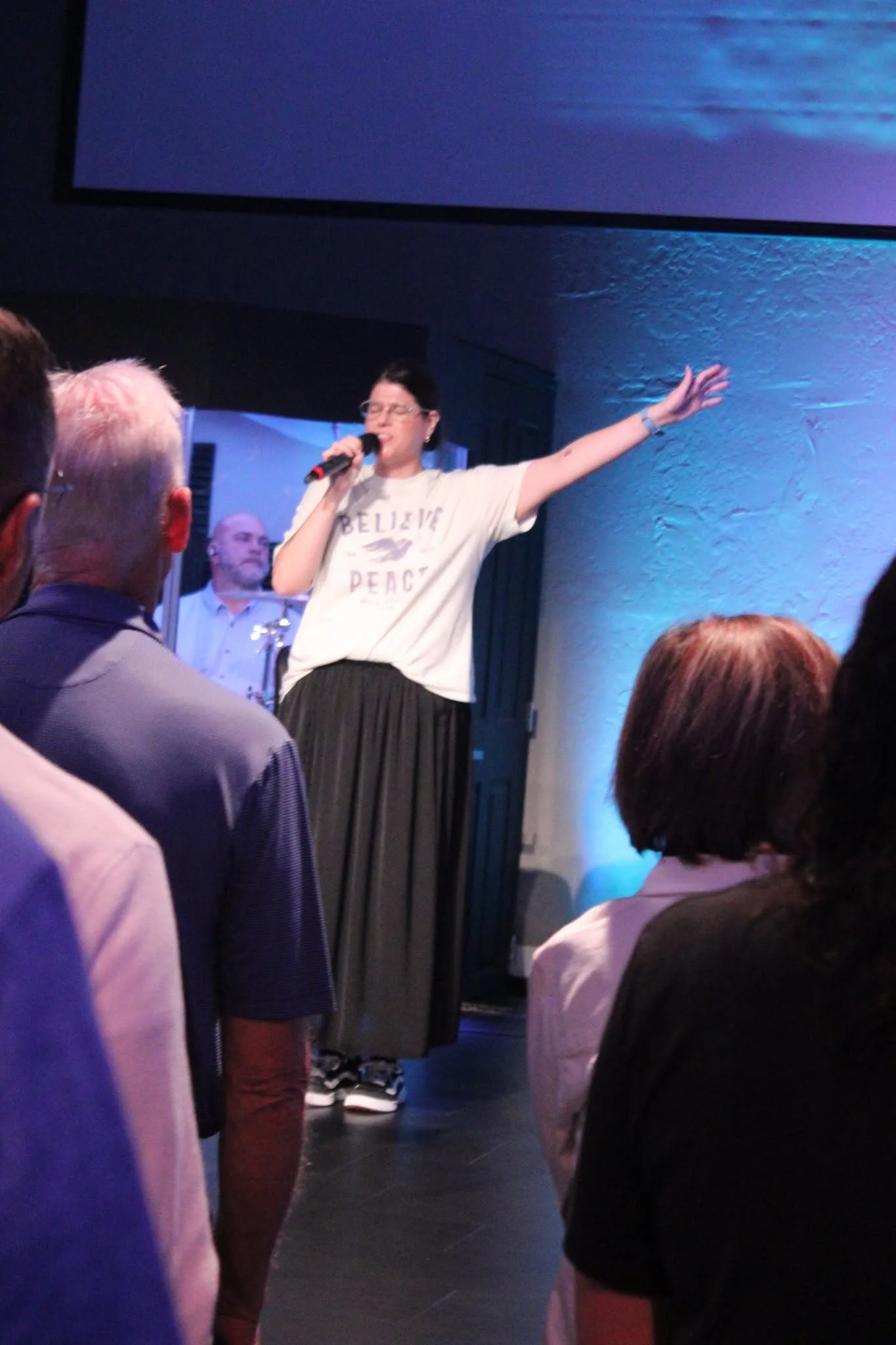 A woman leading from the stage under blue sanctuary light at The Refuge.
