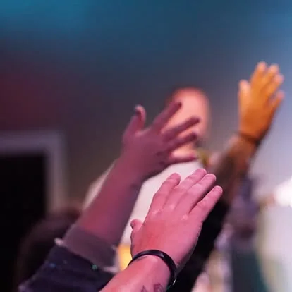 Hands raised in worship under purple and blue sanctuary light at The Refuge.