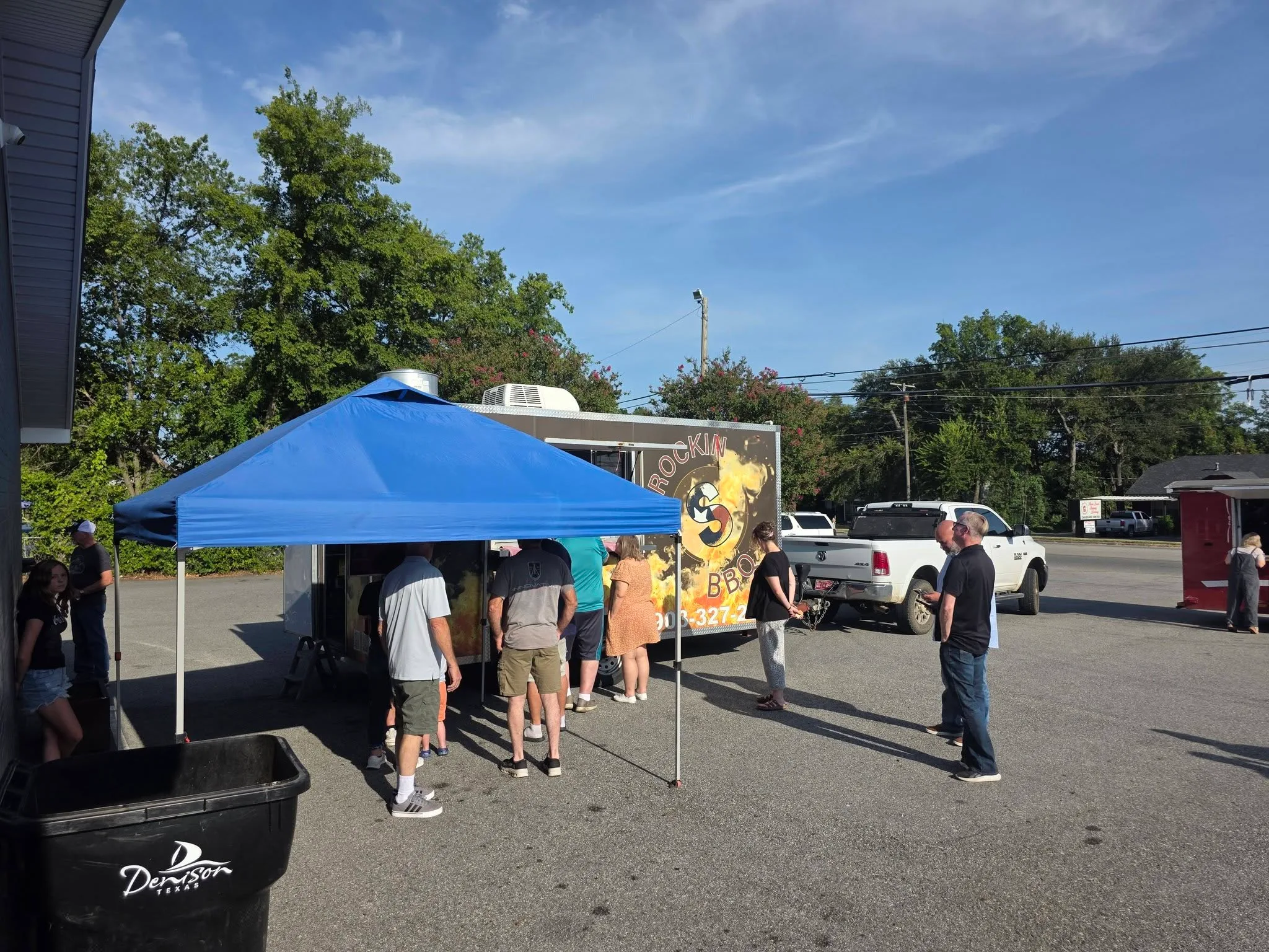 Neighbors gathered under a tent beside a BBQ food truck outside The Refuge.