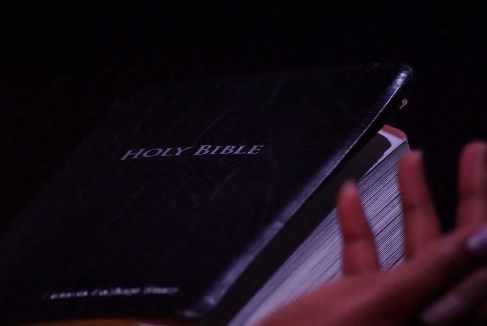 A Holy Bible open in purple sanctuary light during a gathering.